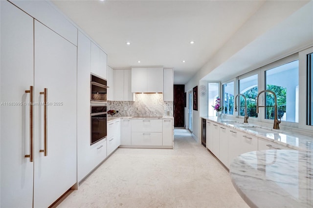 kitchen with sink, backsplash, light stone countertops, black appliances, and white cabinets