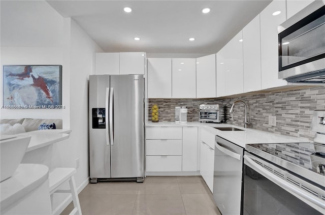 kitchen with light tile patterned floors, appliances with stainless steel finishes, backsplash, white cabinetry, and sink