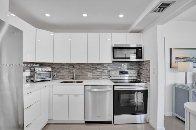 kitchen with decorative backsplash, white cabinets, light tile patterned floors, sink, and stainless steel appliances