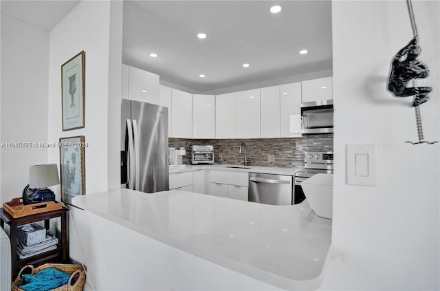 kitchen featuring sink, kitchen peninsula, white cabinetry, stainless steel appliances, and decorative backsplash