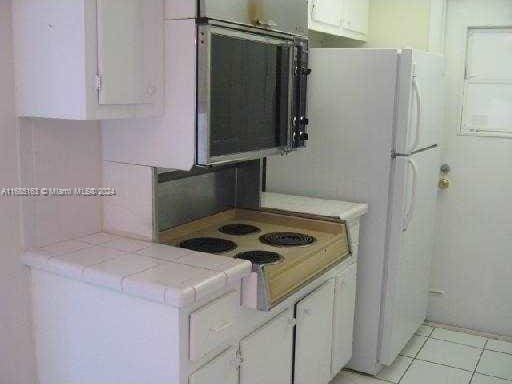 kitchen featuring white electric stovetop, light tile patterned floors, tile counters, and white cabinets