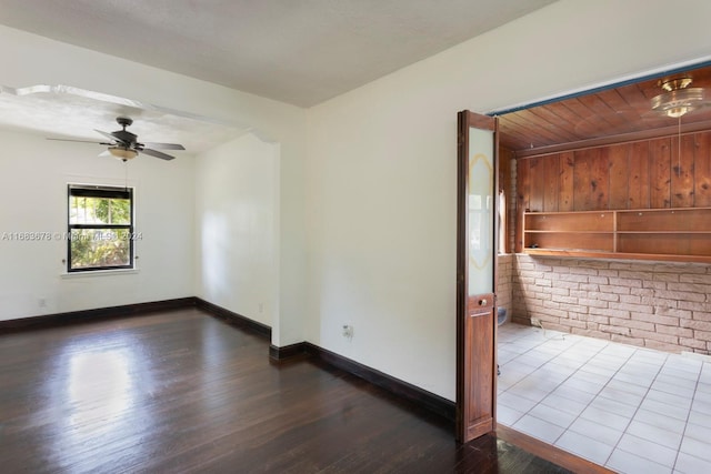 empty room featuring ceiling fan, brick wall, and dark hardwood / wood-style floors