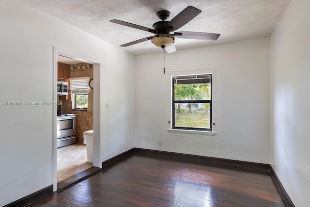 empty room featuring a healthy amount of sunlight, dark wood-type flooring, and ceiling fan