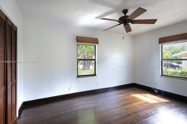 empty room featuring ceiling fan, a healthy amount of sunlight, a textured ceiling, and dark hardwood / wood-style floors