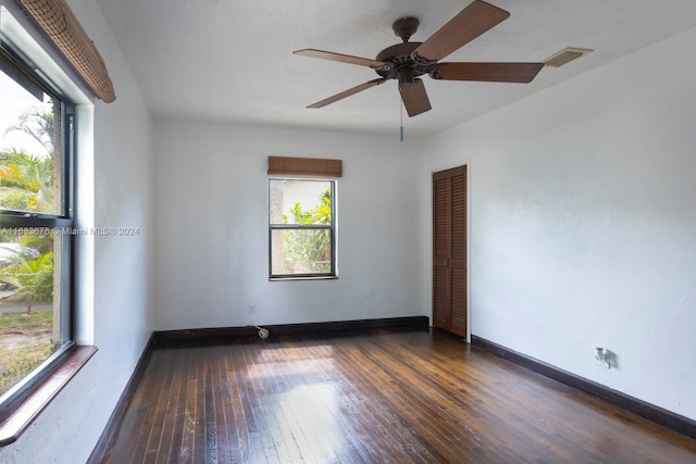 empty room with a healthy amount of sunlight, ceiling fan, and dark hardwood / wood-style flooring