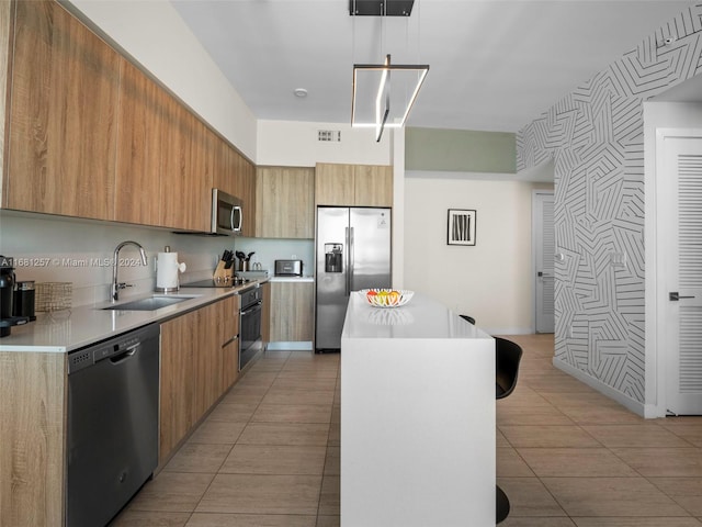 kitchen featuring stainless steel appliances, a center island, sink, light tile patterned floors, and decorative light fixtures