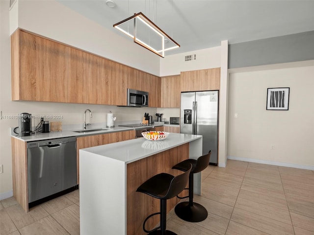 kitchen with stainless steel appliances, light tile patterned floors, sink, a kitchen breakfast bar, and a center island