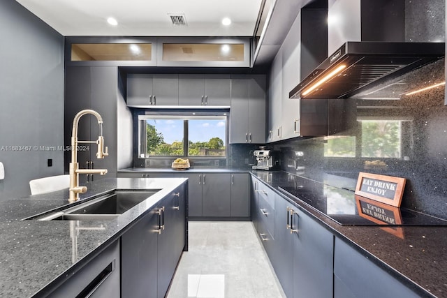 kitchen featuring gray cabinetry, sink, wall chimney exhaust hood, decorative backsplash, and dark stone countertops