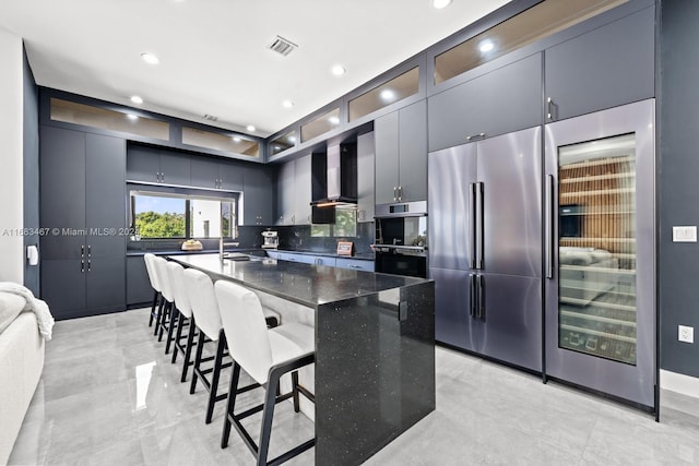 kitchen featuring wall chimney range hood, sink, decorative backsplash, dark stone countertops, and appliances with stainless steel finishes