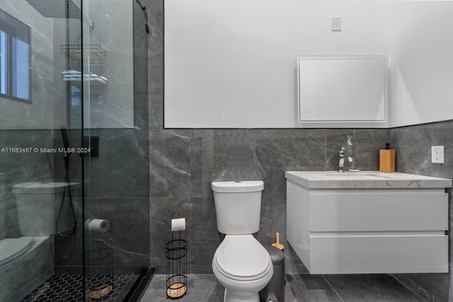 bathroom with tile patterned flooring, toilet, a shower with door, vanity, and tile walls