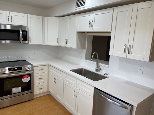 kitchen featuring sink, stainless steel appliances, white cabinetry, and light hardwood / wood-style flooring