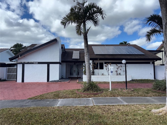 view of front of house featuring stucco siding, fence, solar panels, and roof with shingles