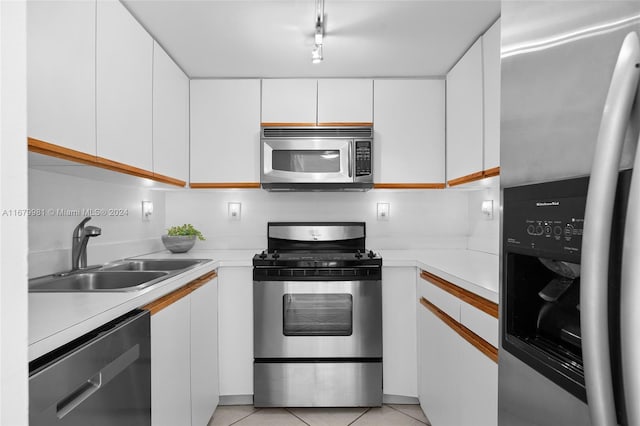 kitchen featuring sink, white cabinetry, rail lighting, stainless steel appliances, and light tile patterned floors