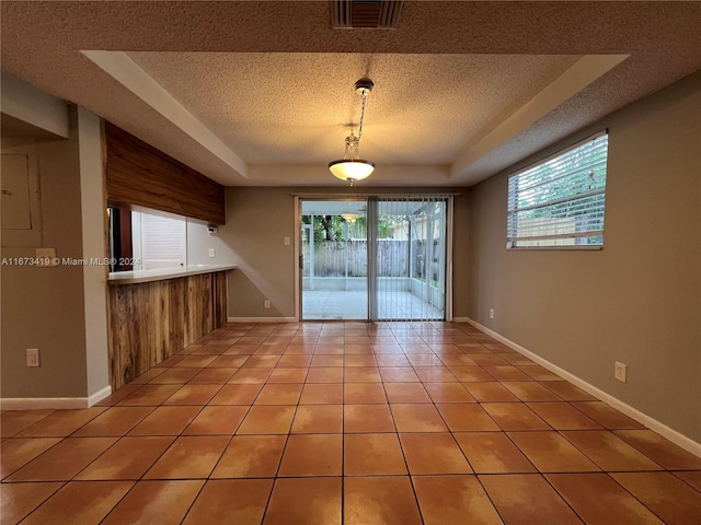 unfurnished dining area featuring a textured ceiling, a tray ceiling, and plenty of natural light