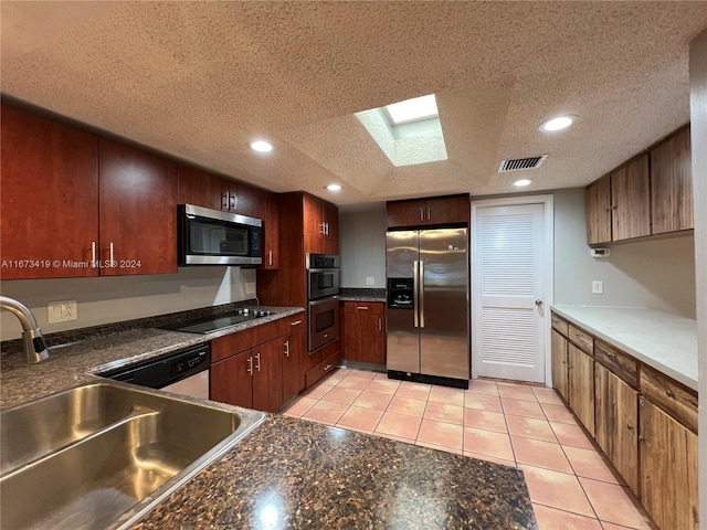 kitchen with sink, light tile patterned flooring, appliances with stainless steel finishes, a textured ceiling, and a skylight