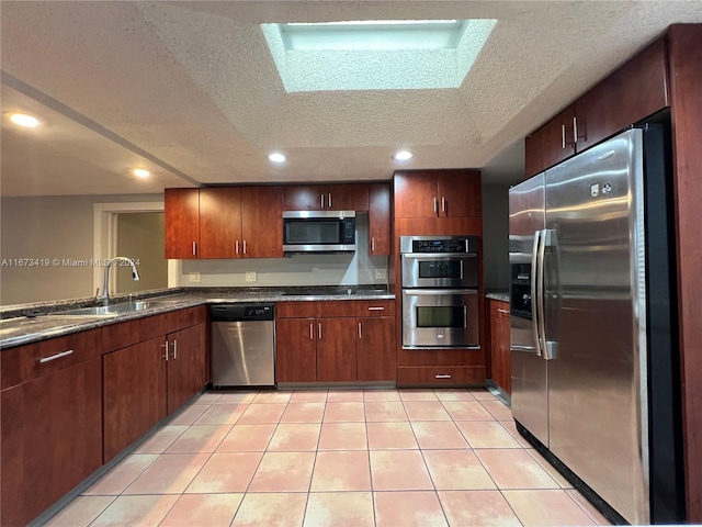 kitchen with sink, a textured ceiling, stainless steel appliances, dark stone countertops, and light tile patterned floors