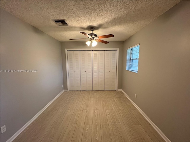 unfurnished bedroom with a closet, a textured ceiling, light hardwood / wood-style floors, and ceiling fan