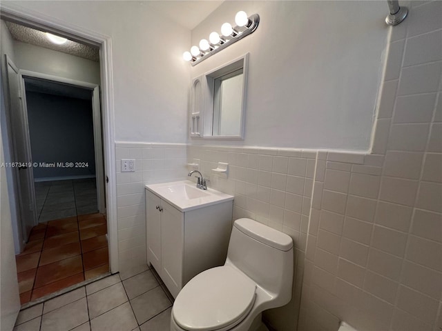 bathroom with tile walls, vanity, toilet, and tile patterned floors