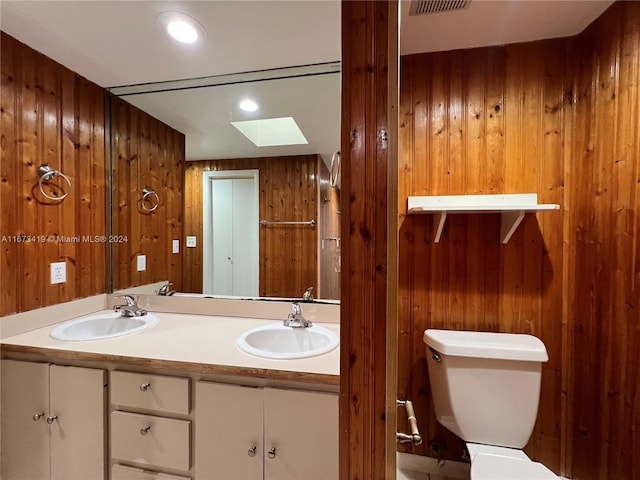 bathroom featuring toilet, wooden walls, vanity, and a skylight