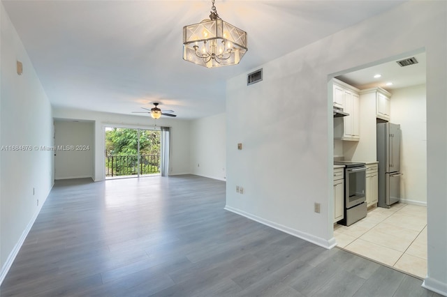 unfurnished living room with ceiling fan with notable chandelier and light hardwood / wood-style flooring