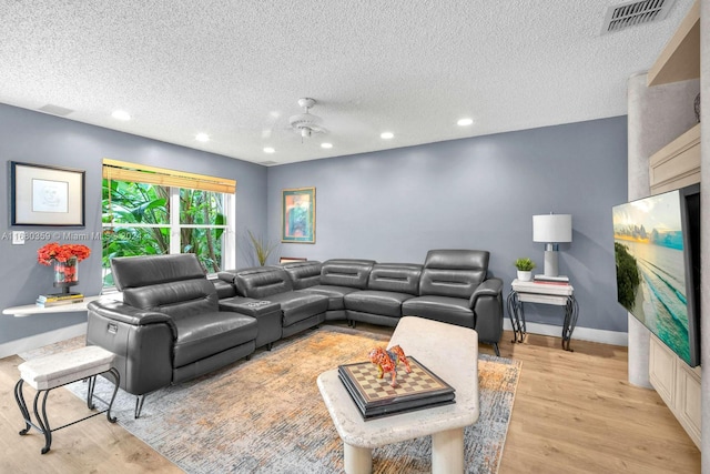 living room featuring a textured ceiling, light wood-type flooring, and ceiling fan