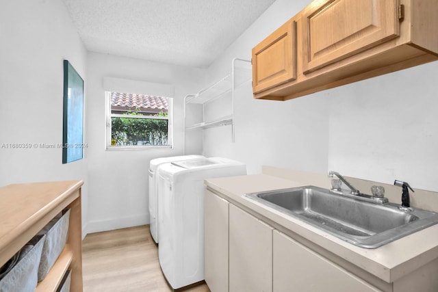 laundry area featuring washing machine and dryer, sink, light wood-type flooring, a textured ceiling, and cabinets