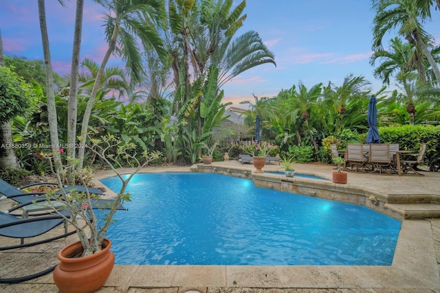 pool at dusk featuring a patio, an in ground hot tub, and pool water feature