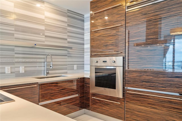 kitchen featuring stainless steel oven, sink, and tile walls