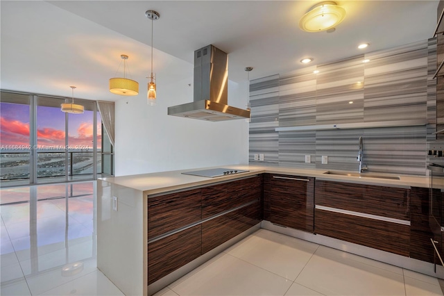 kitchen with black electric stovetop, wall chimney range hood, sink, hanging light fixtures, and light tile patterned floors