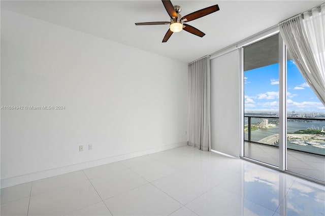 empty room featuring expansive windows, light tile patterned flooring, a water view, and ceiling fan