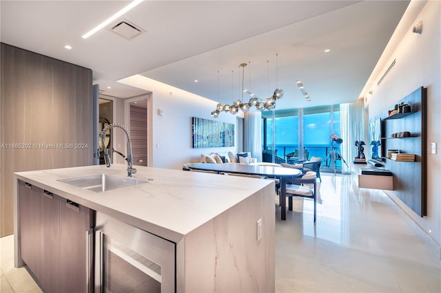 kitchen featuring wine cooler, an island with sink, sink, pendant lighting, and light stone counters