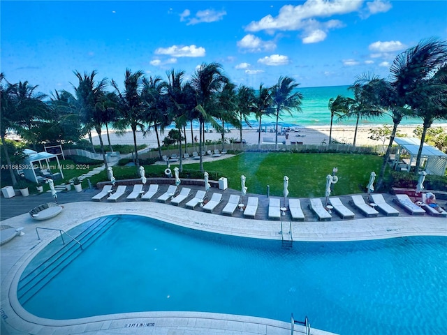 view of swimming pool with a patio, a view of the beach, a lawn, and a water view