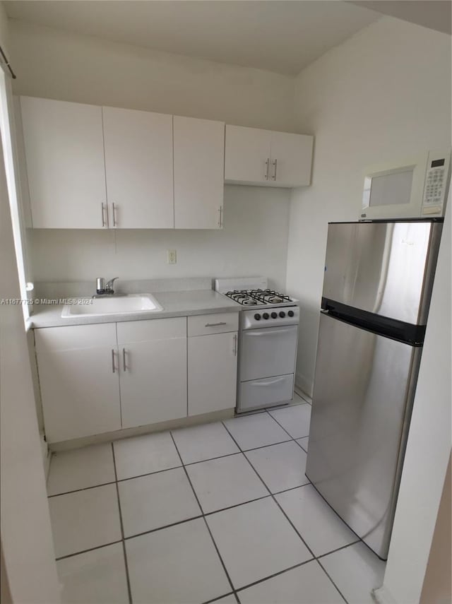 kitchen with white appliances, light tile patterned flooring, white cabinetry, and sink