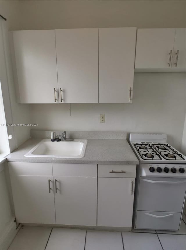 kitchen featuring sink, light tile patterned floors, white range with gas cooktop, and white cabinets