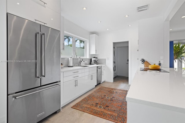 kitchen featuring washer / dryer, sink, appliances with stainless steel finishes, white cabinets, and backsplash