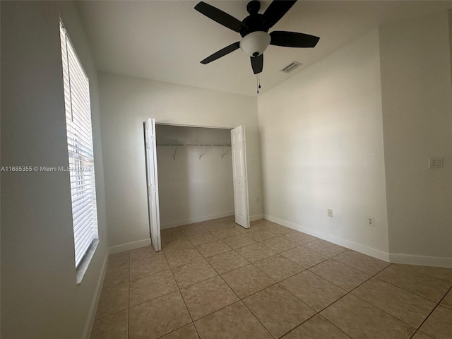 unfurnished bedroom with light tile patterned flooring, multiple windows, ceiling fan, and a closet