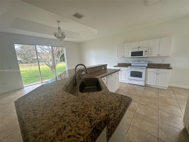 kitchen featuring white cabinets, sink, a kitchen island with sink, a raised ceiling, and white appliances