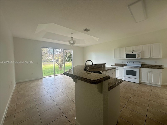 kitchen featuring white cabinetry, sink, a tray ceiling, an island with sink, and white appliances