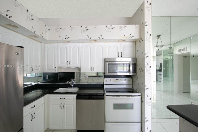 kitchen with appliances with stainless steel finishes, light tile patterned flooring, white cabinetry, and sink