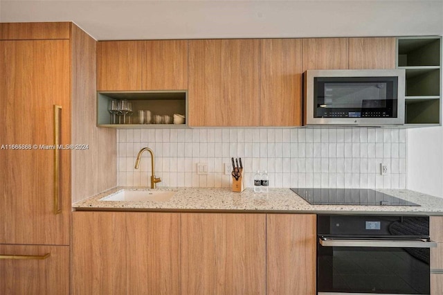 kitchen with sink, black appliances, light stone countertops, and backsplash