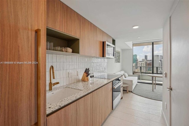 kitchen with decorative backsplash, sink, light tile patterned floors, appliances with stainless steel finishes, and light stone counters