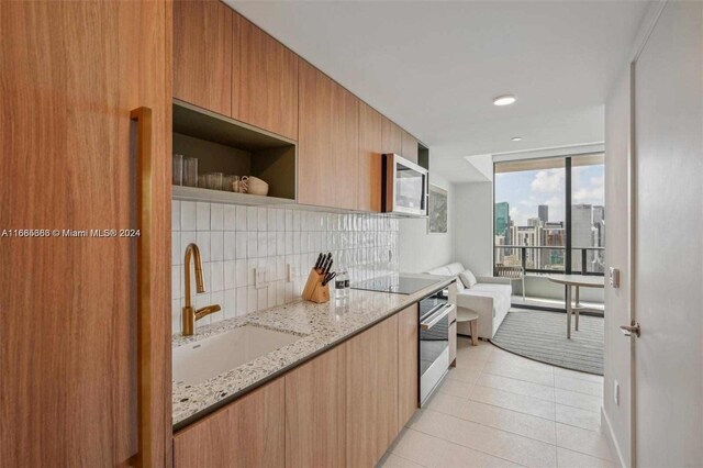 601 Ne 1st 4114, Miami, FL 33132 - kitchen featuring a sink, stainless steel appliances, backsplash, light tile patterned floors, and light stone countertops