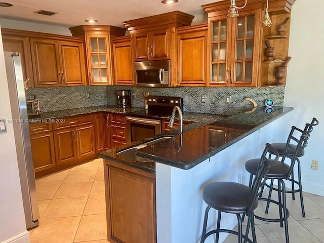 kitchen featuring stainless steel appliances, a kitchen breakfast bar, backsplash, kitchen peninsula, and dark stone countertops