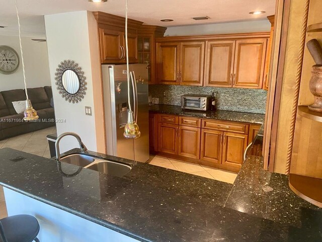 kitchen featuring dark stone counters, sink, kitchen peninsula, decorative backsplash, and stainless steel fridge with ice dispenser