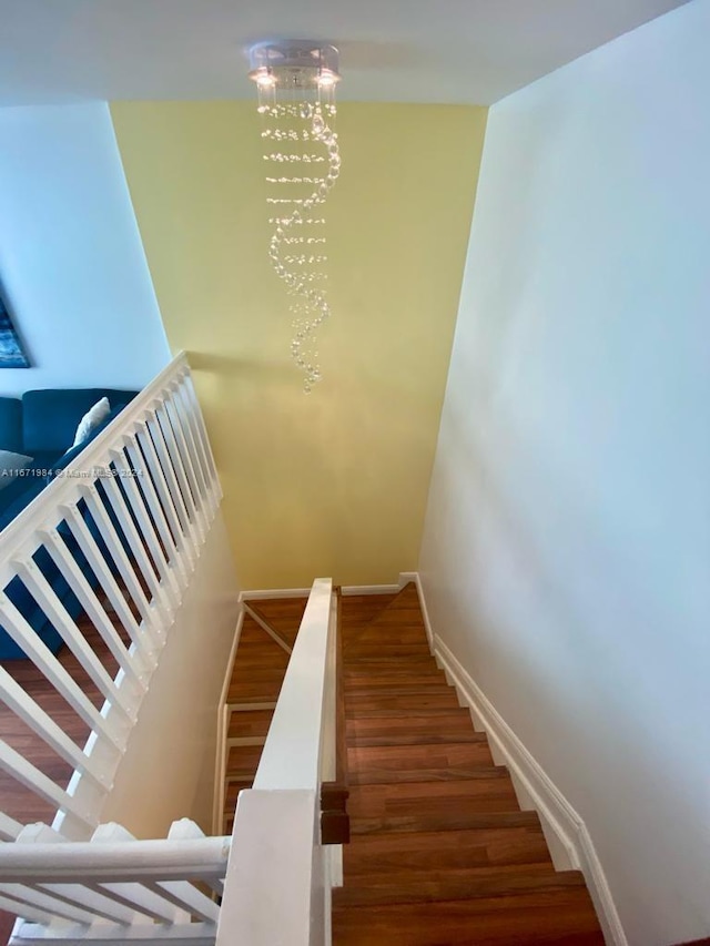 stairway featuring wood-type flooring and an inviting chandelier