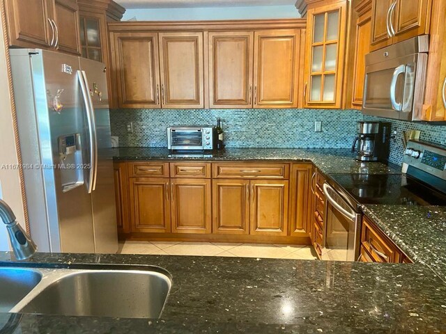 kitchen with sink, stainless steel appliances, backsplash, dark stone counters, and light tile patterned floors