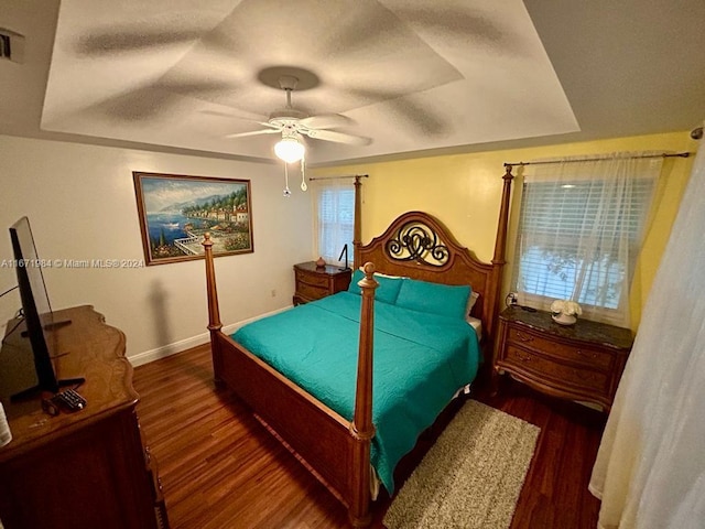 bedroom featuring ceiling fan, dark hardwood / wood-style flooring, and a tray ceiling