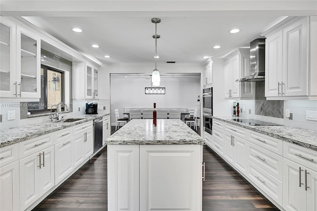 kitchen featuring a kitchen island, decorative light fixtures, white cabinetry, stainless steel appliances, and wall chimney range hood