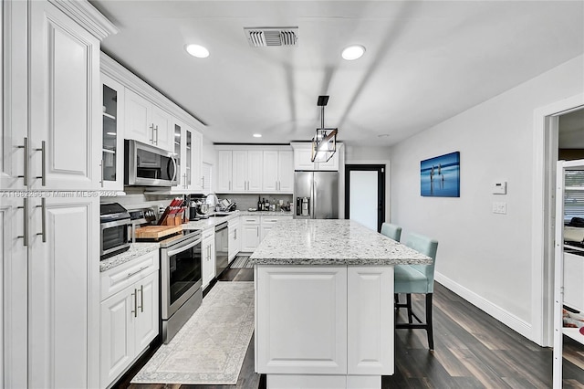 kitchen featuring white cabinetry, light stone counters, decorative light fixtures, a center island, and appliances with stainless steel finishes