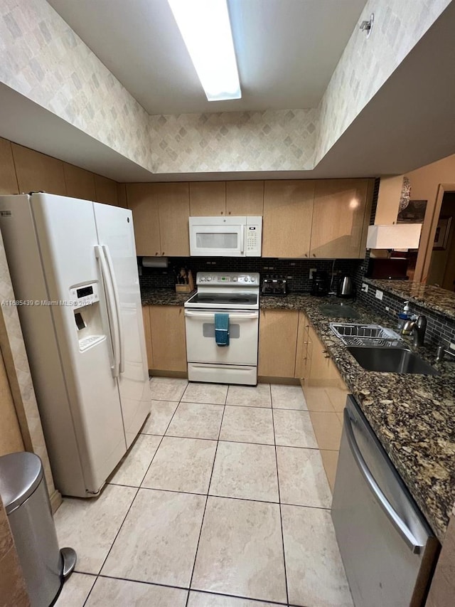 kitchen with tasteful backsplash, white appliances, sink, dark stone countertops, and light tile patterned flooring